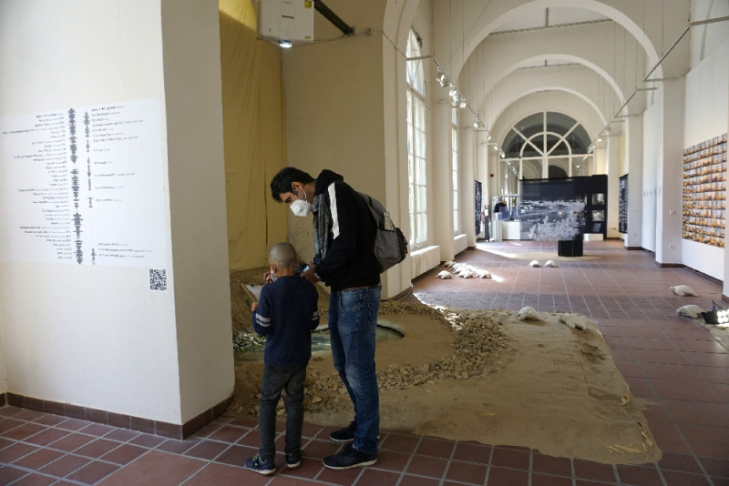 Ein Mann und ein Kind studieren ein Kunstwerk, das aus Sand und Wasser besteht.