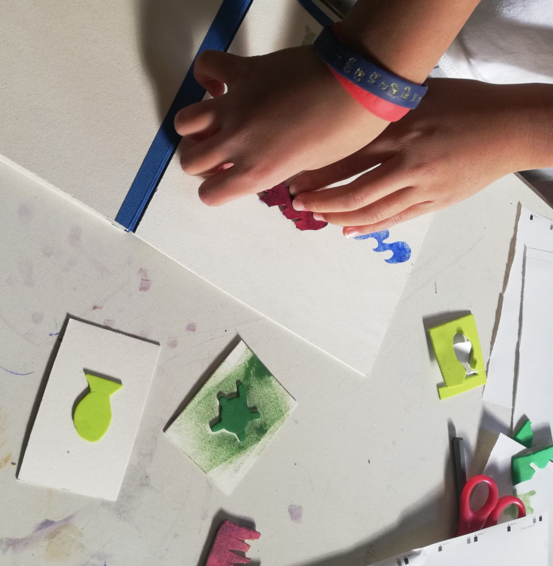 Zwei Kinderhände kleben eine bunte Schablone auf weiße Pappe