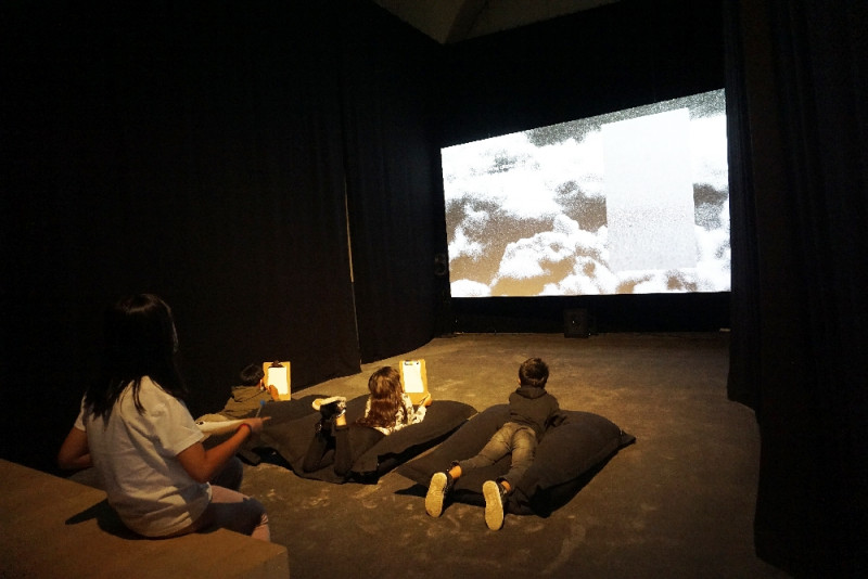 Vier Schüler:innen sind in einem abgedunkelten Raum und schauen einen Film auf einer Leinwand an.