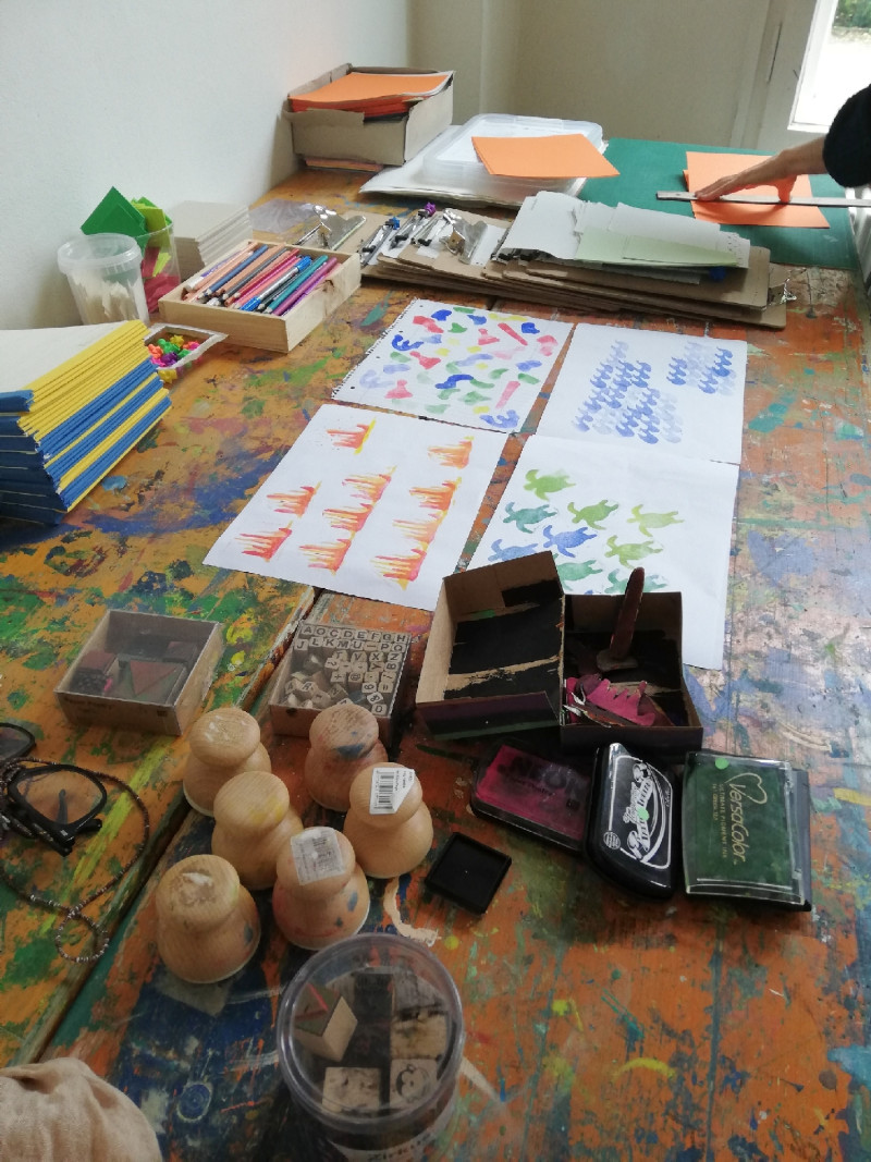 Auf einem Arbeitstisch liegen Stempel, Stempelkissen, Farbproben der Stempel auf Papier