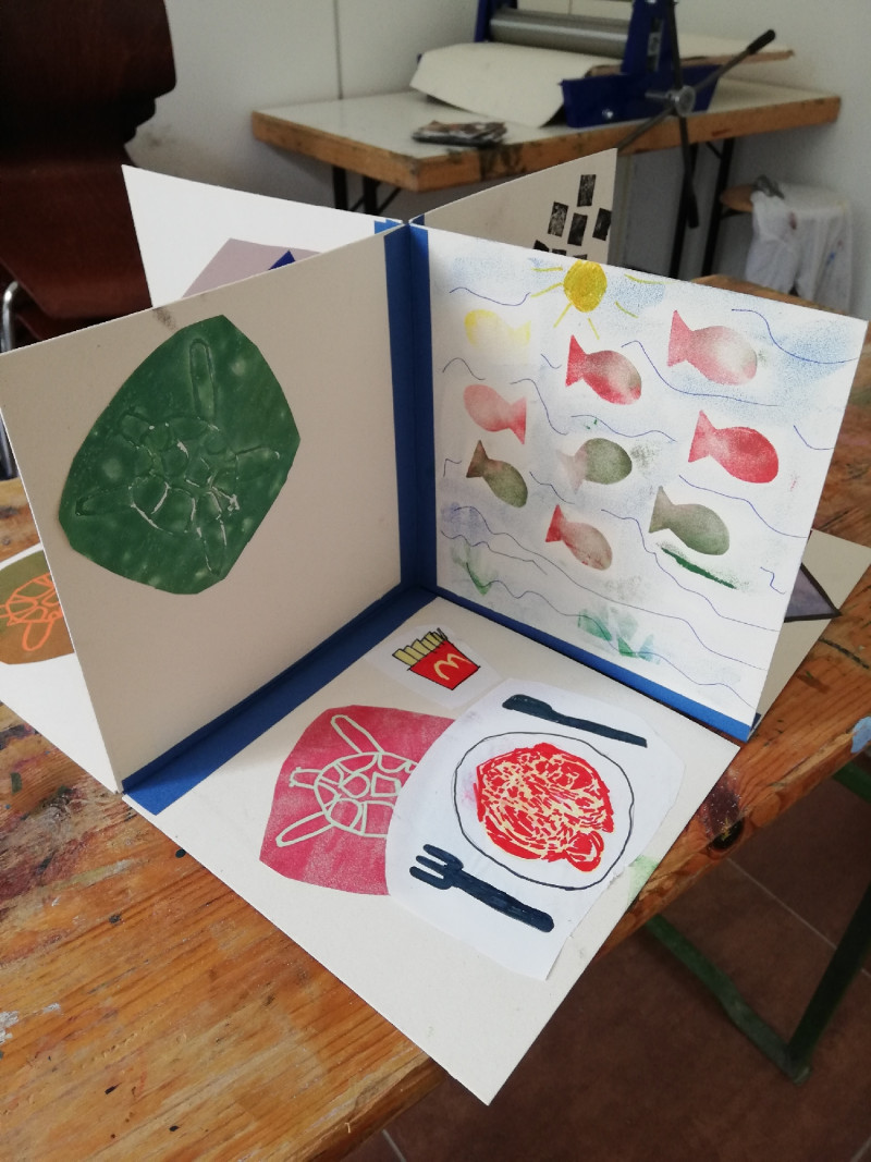 Ein bunt bedrucktes Buch, das aufgeklappt aussieht wie ein Raum mit Boden und zwei Wänden