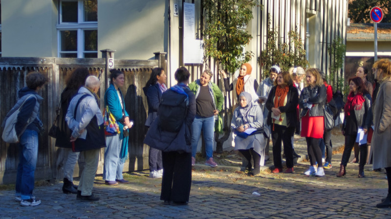 Eine große Gruppe Menschen stehen vor einem Gebäude und hören eine Person zu.