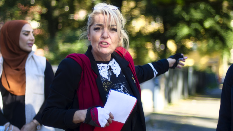 Eine Frau schaut in die Kamera und zeigt auf etwas hinter ihr.