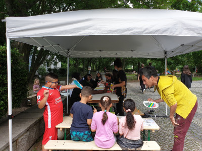 Kinder sitzen unter einem Partypavillon auf Bierbänken und malen