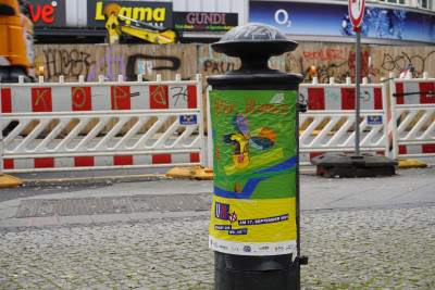 Buntes Plakat auf Hydrantem, Baustelle ist im Hintergrund zu sehen