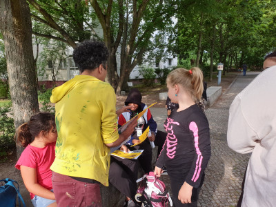 Kinder sitzen und stehen und schauen sich Bilder an, die ein Künstler ihnen zeigt