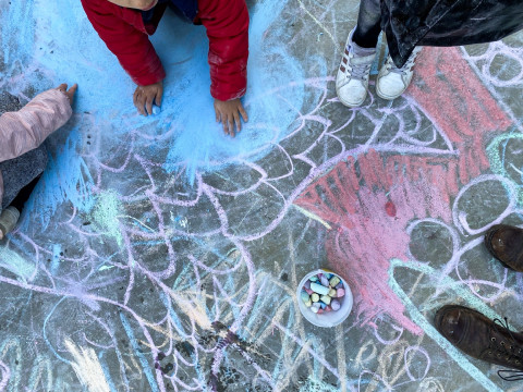 Kinder malen mit bunter kreide große, wilde Zeichnungen auf den Boden.