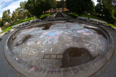 Großer leerer, runder Springbrunnen ist mit großen, bunten Kreidezeichnungen bemalt.