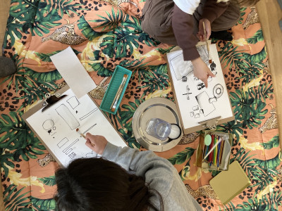 Zwei junge Personen sitzen auf einer bunten Picknickdecke und zeichnen