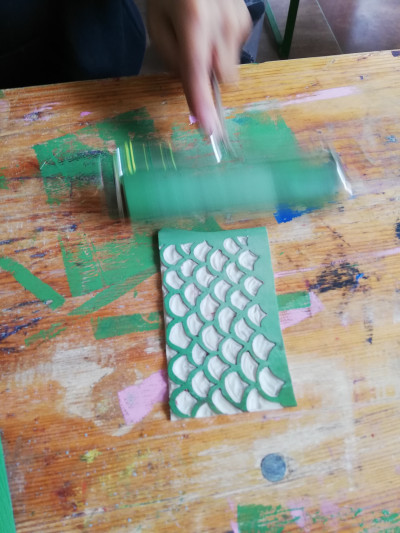 Grüne Farbrolle wird auf Holztoisch von Hand über Linolplatte gerollt