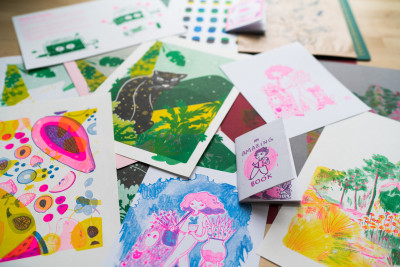Leuchtend bunte Papierbilder mit Zeichnungen liegen verstreut auf einem Tisch