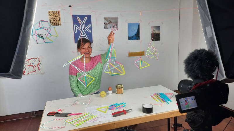 Weibliche Person sitzt an einem Tisch und hält dreidimensionale figur aus bunten Strohhalmen hoch